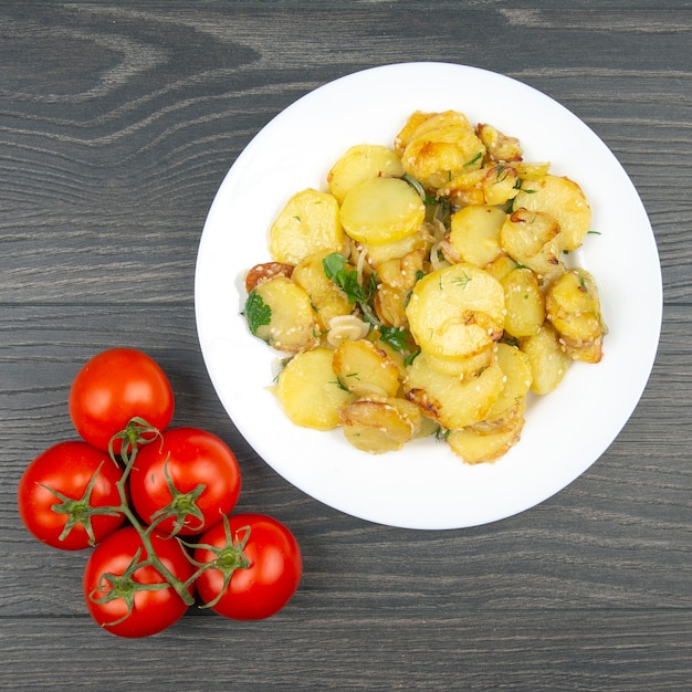 Gotowane smażone ziemniaki z ziołami i warzywami w białym talerzu na drewnianym stole