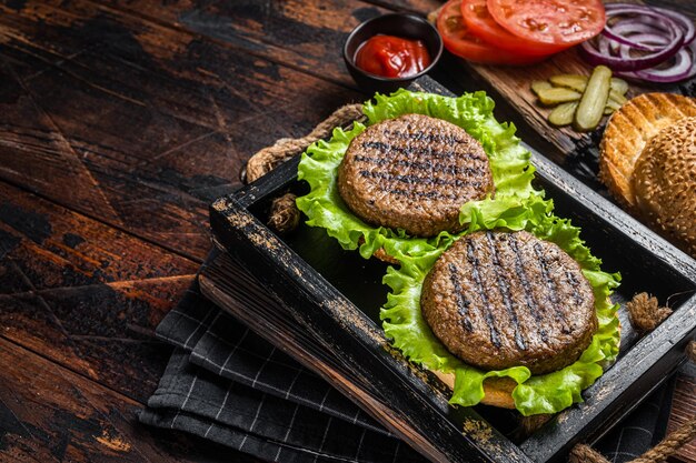 Zdjęcie gotowanie bezmięsne burgery na bazie roślinnej z wegetariańskimi bezmięsnymi pieczonymi kotletami, pasztecikami, pomidorem i cebulą w drewnianej tacy do serwowania. drewniane tło. widok z góry. skopiuj miejsce.