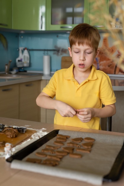 Gotowanie ciasteczek w domu na Wielkanoc rudowłosy chłopiec w żółtej koszulce gotuje w kuchni pionowe zdjęcie