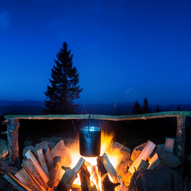 Gotowanie jedzenia w garnku w ogniu pod błękitnym nocnym niebem z wieloma gwiazdami
