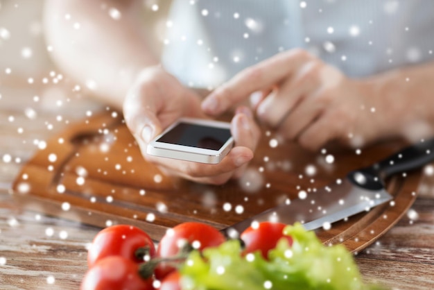 gotowanie, ludzie, technologia i koncepcja domu - zbliżenie człowieka czytającego przepis ze smartfona i warzyw na stole w kuchni