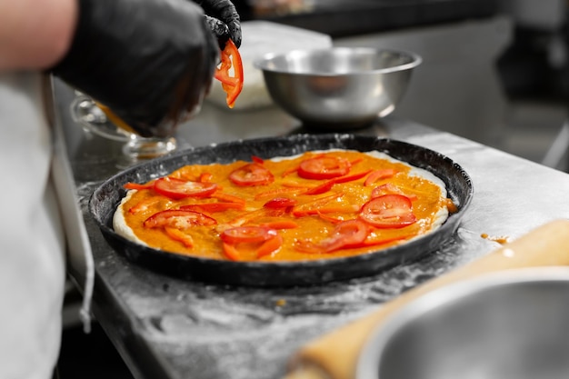 Gotowanie pizzy. Zbliżenie dłoni szefa kuchni rozprowadzającej plasterki pomidora na cieście.