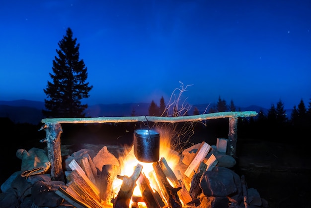 Gotowanie potraw w garnku na ogniu pod błękitnym nocnym niebem z wieloma gwiazdami