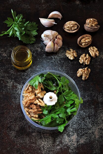 Gotowanie sosu pesto z natką pietruszki i orzechami włoskimi. Przepis na pesto z orzecha włoskiego. Składniki na pesto w filiżance blendera. Widok z góry.