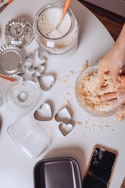 Zdjęcie gotowanie z bliska. biały stół z narzędziami do pieczenia. formy do ciastek i formy do pieczenia. ręce kobiet ugniatają ciasto w misce. pojęcie działalności kulinarnej i posiłku.