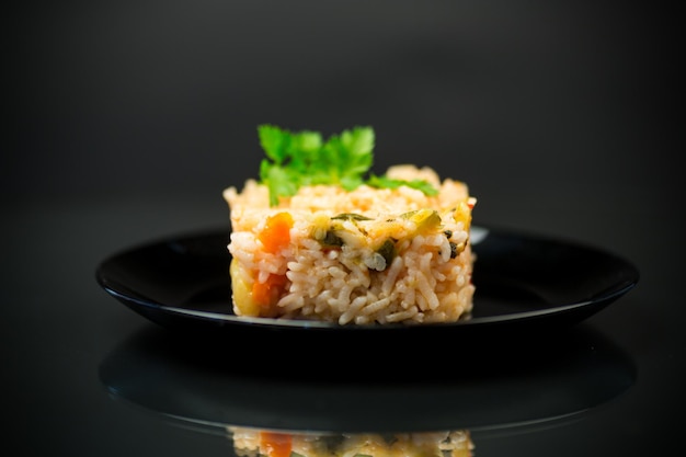 Gotowany ryż z cukinią, marchewką i warzywami na talerzu izolowanym na czarnym tle