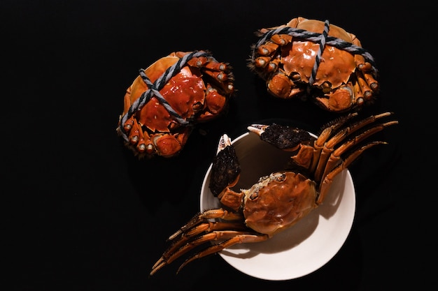 Gotowany Szanghaj włochaty krab lub chiński mitenka krab (Eriocheir sinensis) z chili i ziołami na czarnym tle
