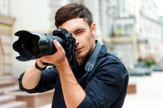 Gotowy do strzału. Pewny siebie młody człowiek fotografujący coś stojąc na zewnątrz