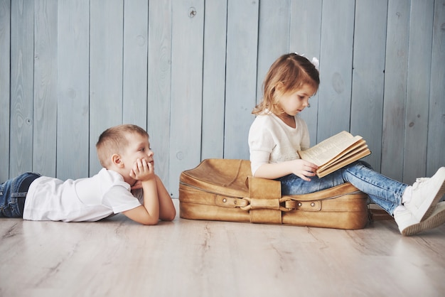 Gotowy do wielkiej podróży. Szczęśliwa mała dziewczynka i chłopiec czyta intereting książkę niosącą dużą teczkę i ono uśmiecha się. Podróż, wolność i wyobraźnia