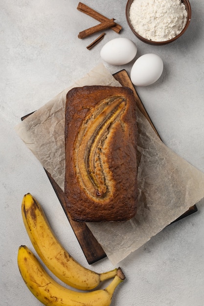 Gotowy świeży chleb bananowy w prostokątnym naczyniu do pieczenia ze składnikami na jasnym tle