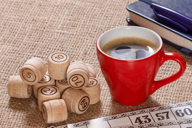 Zdjęcie gra planszowa lotto na worze. drewniane beczki lotto i karty do gry w lotto z filiżanką kawy i notesem z długopisem w tle.