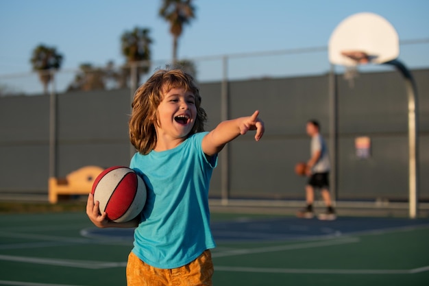 Gra w koszykówkę dla dzieci Śliczny mały chłopiec śmiejący się i trzymający piłkę do koszykówki, próbujący zdobyć wynik śmiejąc się Dziecko wskazujące gestem
