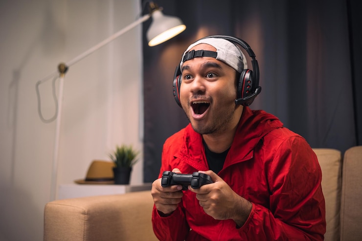 Zdjęcie gra wideo młody azjatycki przystojny mężczyzna siedzi na kanapie trzymając joystick w salonie szczęście streamer indyjski mężczyzna nosi zestaw słuchawkowy gra online w ciemni