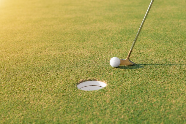 Gracz golfa przy kładzeniem uderza piłkę golfową w dziury zieleni. Zamknij się w golfa i putter.