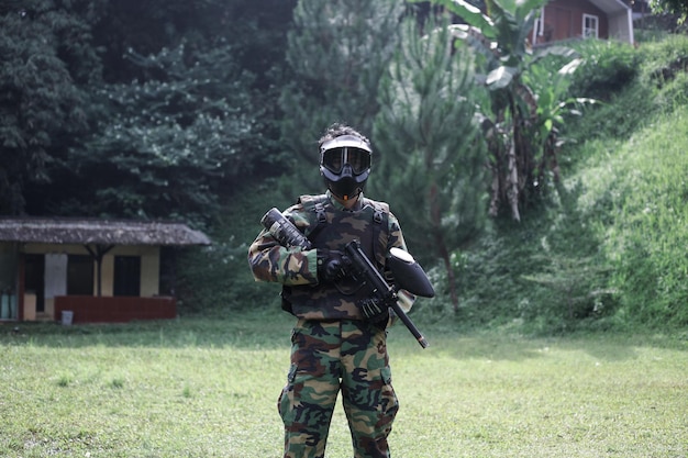 Gracz paintballa trzymający broń w mundurze kamuflażowym