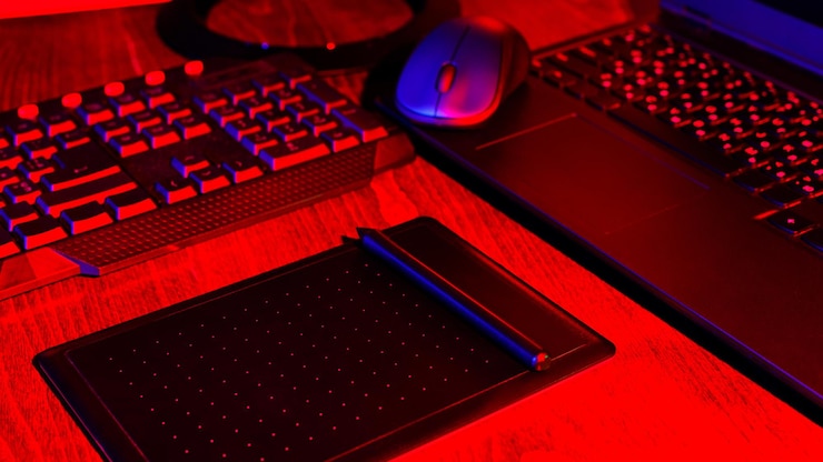 Grafik w miejscu pracy w neonowym świetle. Sprzęt komputerowy i tablet graficzny do tworzenia treści. Domowe biuro freelancera w różowym, niebieskim świetle. Koncepcja biura domowego
