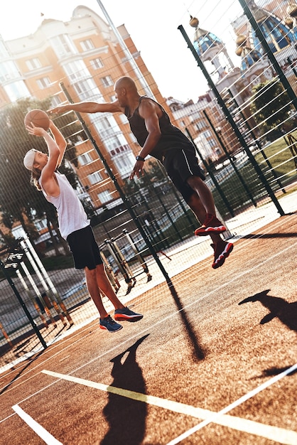 Zdjęcie grając ciężko. dwóch młodych mężczyzn w sportowej odzieży grających w koszykówkę podczas spędzania czasu na świeżym powietrzu