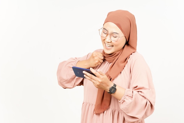 Grając w grę mobilną na smartfonie pięknej azjatyckiej kobiety noszącej hidżab na białym tle