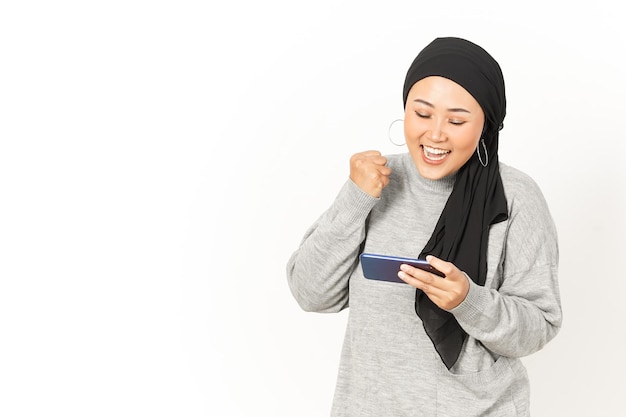 Granie w grę mobilną na smartfonie pięknej azjatyckiej kobiety noszącej hidżab na białym tle