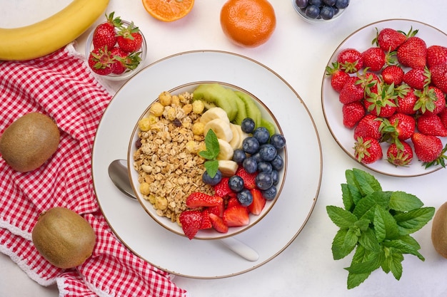 Granola z truskawkami, kiwi, bananem i borówkami na okrągłym talerzu na białym stole