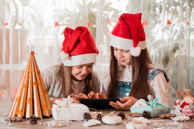 Gratulacje W Kwarantannie. Dziewczyny W świątecznych Dekoracjach Komunikują Się Ze Swoimi Rodzinami Za Pośrednictwem Tabletu.