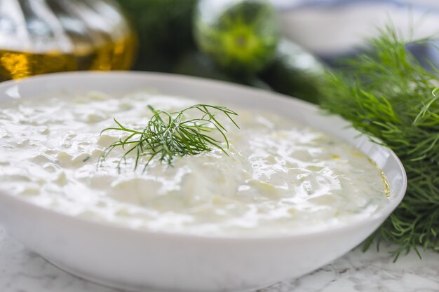 Grecki dip lub dressing tzatziki przygotowane z ogórkiem, śmietaną jogurtową oliwą i świeżym koprem