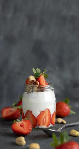 Greckie jogurty, orzechy i truskawki w szklanym słoju na szarym stole z łyżką z bliska miejsca na kopię