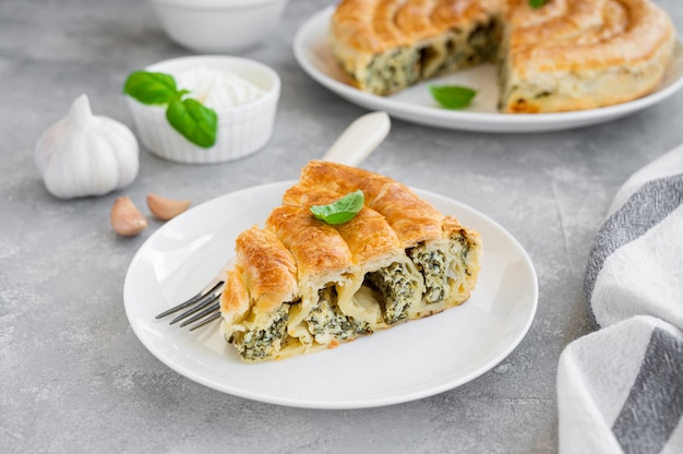 Greckie Spanakopita Ciasto Z Serem Feta I Szpinakiem Na Białym Talerzu Na Szarym Tle Betonu. Skopiuj Miejsce.