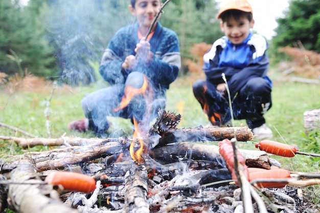 Grill w naturze, grupa ludzi przygotowująca kiełbaski w ogniu (uwaga: płytkie dof)