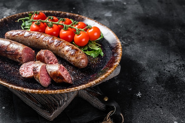 Grillowana kiełbasa bawarska z rukolą i pomidorem na talerzu. Czarne tło. Widok z góry. Skopiuj miejsce.