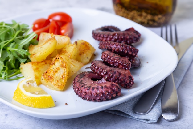 Grillowana Ośmiornica Ze Smażonymi Ziemniakami, Rukolą, Pomidorami I Cytryną. Zbliżenie.