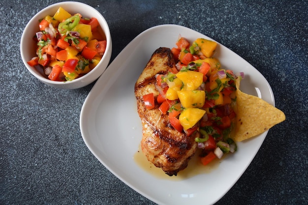 Grillowana pierś z kurczaka z pikantną salsą, mango, ziołami, cebulą i papryką, chipsami kukurydzianymi. Meksykańskie jedzenie.