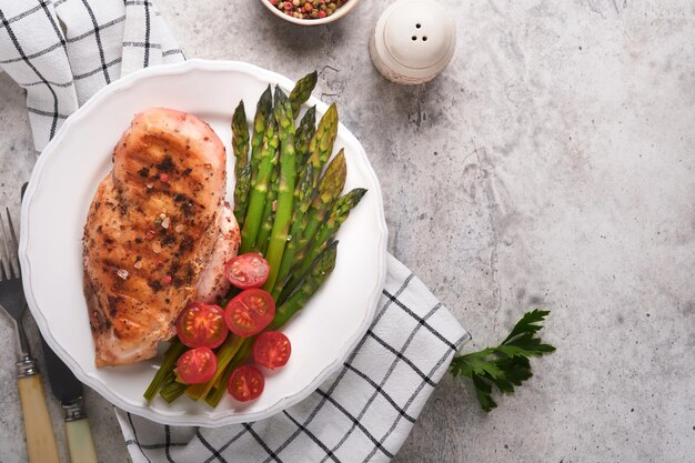 Grillowana pierś z kurczaka z warzywami Grillowany stek z kurczaka, szparagi i pomidorki koktajlowe w czarnym talerzu na jasnoszarym betonowym tle stołu Zdrowy dietetyczny lunch Smażony stek z grilla Widok z góry