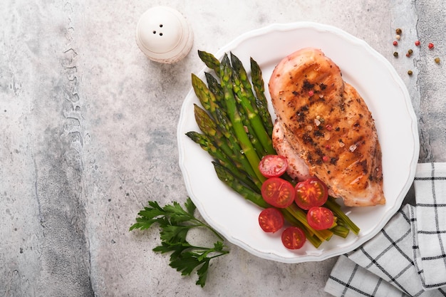 Grillowana pierś z kurczaka z warzywami Grillowany stek z kurczaka, szparagi i pomidorki koktajlowe w czarnym talerzu na jasnoszarym betonowym tle stołu Zdrowy dietetyczny lunch Smażony stek z grilla Widok z góry