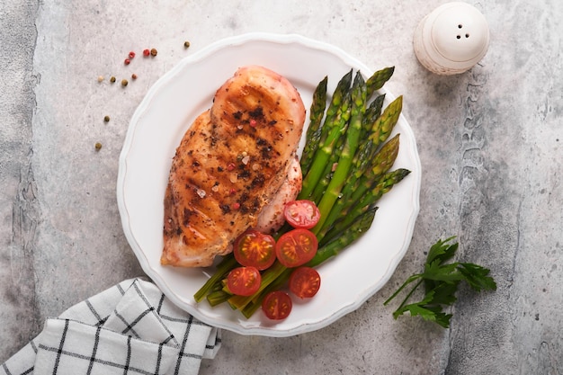 Grillowana pierś z kurczaka z warzywami Grillowany stek z kurczaka, szparagi i pomidorki koktajlowe w czarnym talerzu na jasnoszarym betonowym tle stołu Zdrowy dietetyczny lunch Smażony stek z grilla Widok z góry