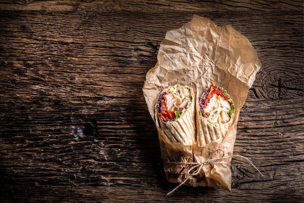 Zdjęcie grillowana tortilla wraps z kurczakiem i warzywami zawinięta w papier, ułożona na rustykalnym drewnie.