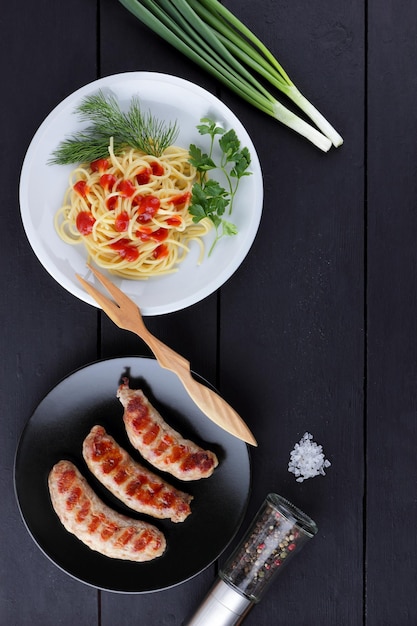 Grillowane kiełbaski na ciemnym tle Spaghetti z sosem i zielenią na białym talerzu Makaron i danie mięsne na grillu Widok z góry