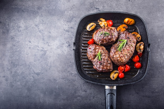 Grillowane steki wołowe na grillowanej patelni z pieczarkami, pomidorami i rozmarynem.