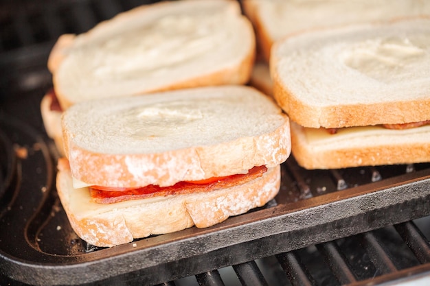 Grillowanie kanapki z serem z grilla z paskami boczku i świeżym pomidorem na grillu gazowym na świeżym powietrzu.