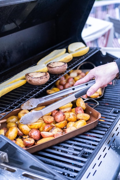 Grillowanie małych ziemniaków z plastrami czosnku na zewnętrznym grillu gazowym.