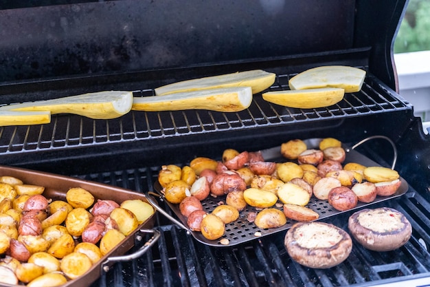 Grillowanie małych ziemniaków z plastrami czosnku na zewnętrznym grillu gazowym.