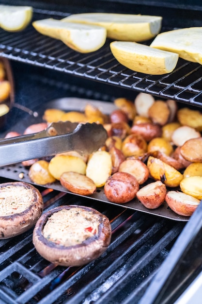 Grillowanie małych ziemniaków z plastrami czosnku na zewnętrznym grillu gazowym.