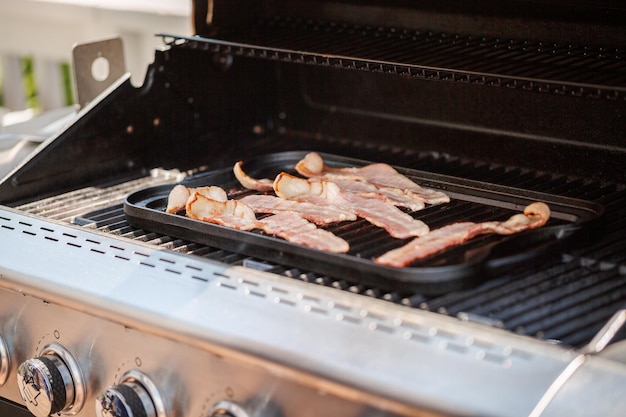 Grillowanie pasków boczku na żeliwnej patelni w zewnętrznym grillu gazowym.