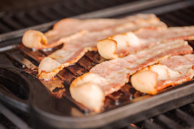 Grillowanie pasków boczku na żeliwnej patelni w zewnętrznym grillu gazowym.