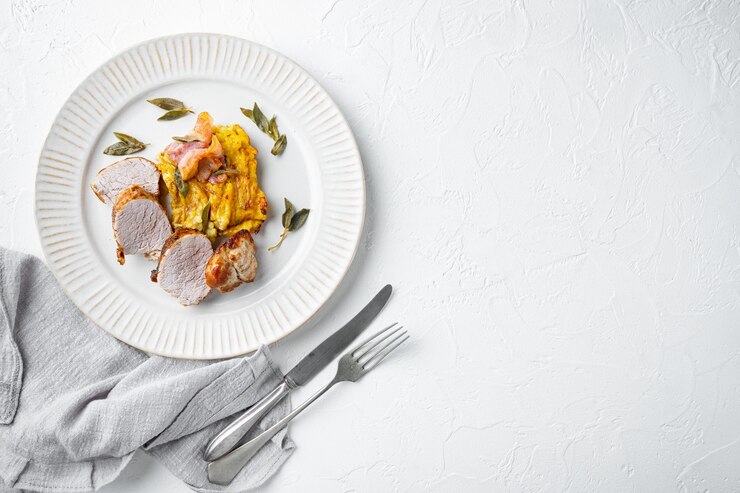 Grillowany filet wieprzowy i zapiekanka ziemniaczana z szałwią i zestawem prosciutto, na talerzu, na białym kamiennym stole, płaski widok z góry
