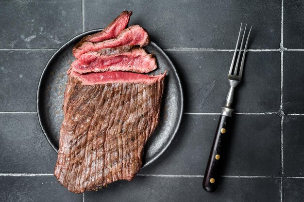 Zdjęcie grillowany flap lub flank steak pocięty na talerzu czarne tło górny widok
