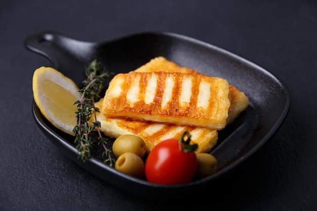 Grillowany ser halloumi na czarnej patelni z oliwkami pomidory ogórki tymianek i cytryna Tradycyjny ser wschodniośródziemnomorski Czarne tło selektywne focus zbliżenie