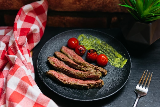 Grillowany stek Picanha z sosem chimichurri i pomidorkami koktajlowymi na czarnym talerzu