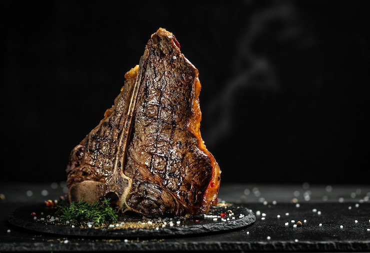Zdjęcie grillowany stek t-bone na kamiennym stole. soczysty stek rzadka wołowina z przyprawami na czarnym stole, baner, menu, przepis, miejsce na tekst...