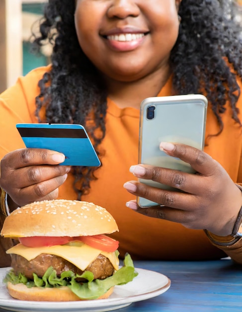 Gruba kobieta używająca telefonu i karty kredytowej z hamburgerem na stole koncepcja zakupów na dostawę